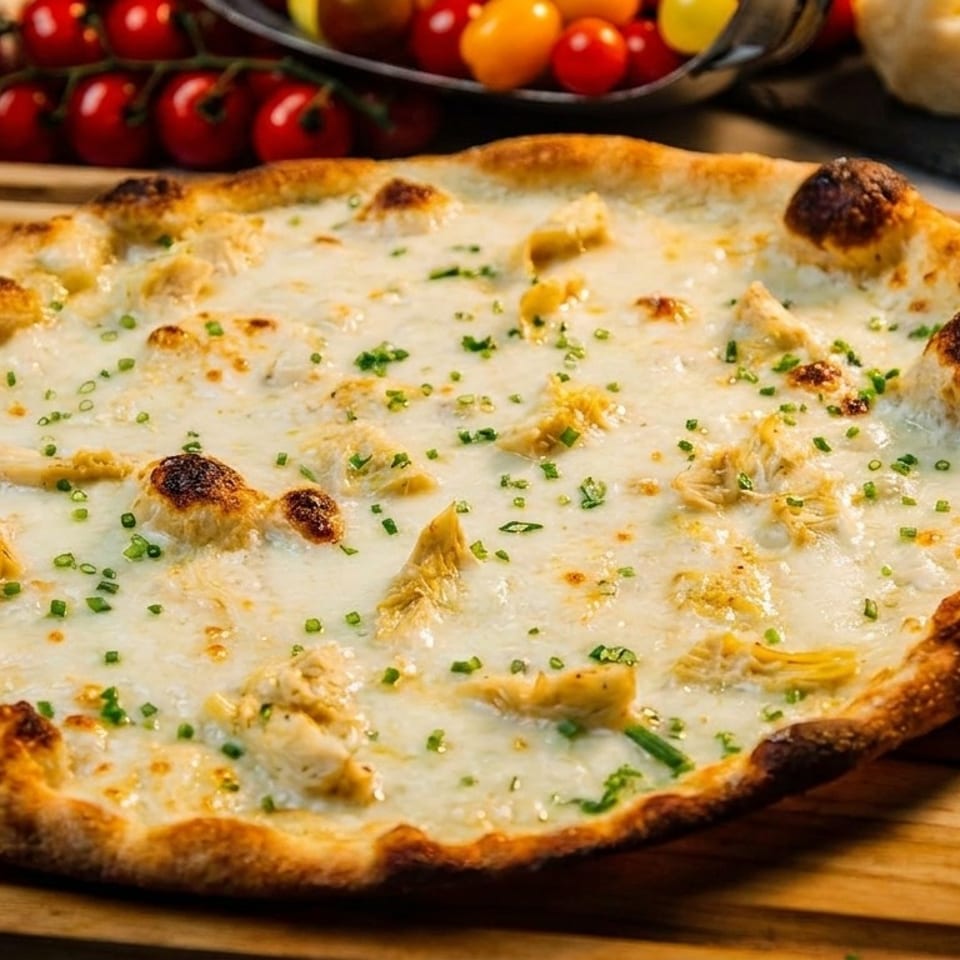 White pizza with chicken, artichoke hearts, and chives on a wooden board.